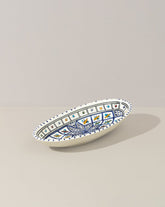 A hand painted decorative oval ceramic plate with a geometric pattern, predominantly white with blue and gold accents.